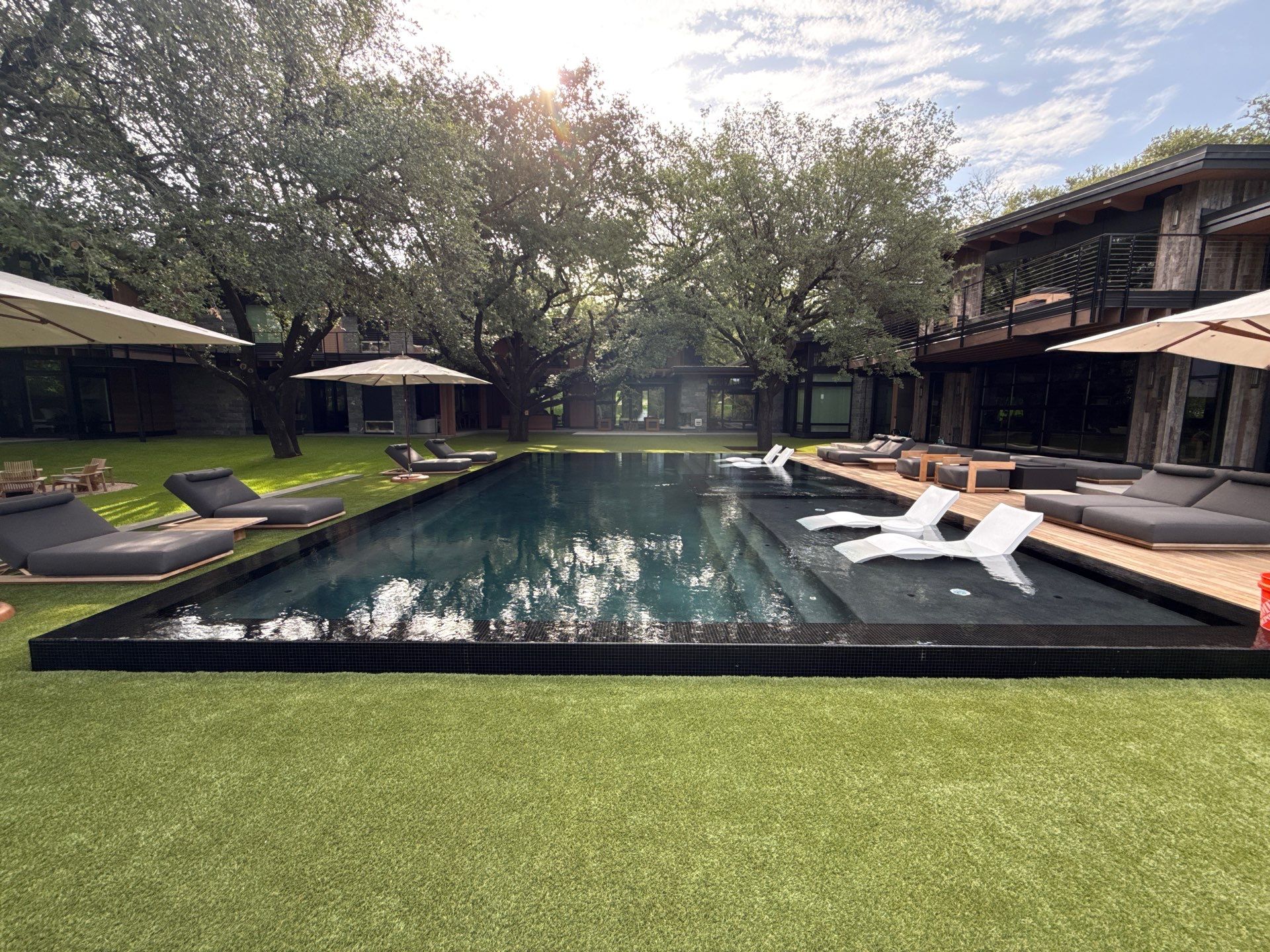 Perimeter Overflow Pool and Spa in Plano, TX with Bisazza black mosaic tile, black pebble plaster, with Ipe wood deck and artificial turf decking.